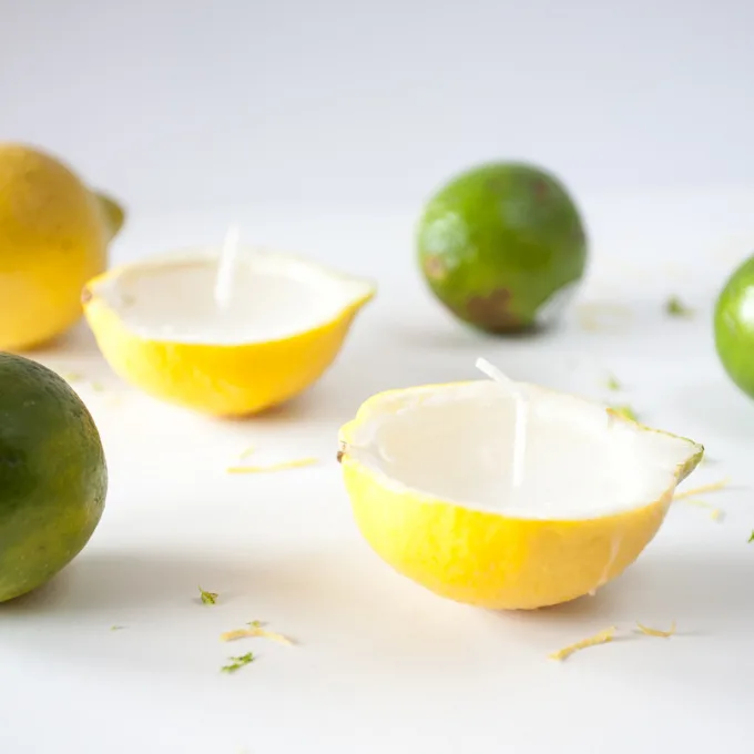 Two lemon rind candles surrounded by green limes on a white backdrop