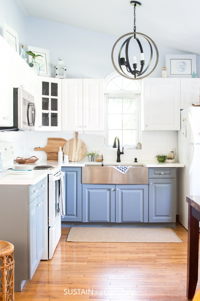 A coastal cottage kitchen with high ceilings, white and gray cabinets and dark fixtures and accessories 