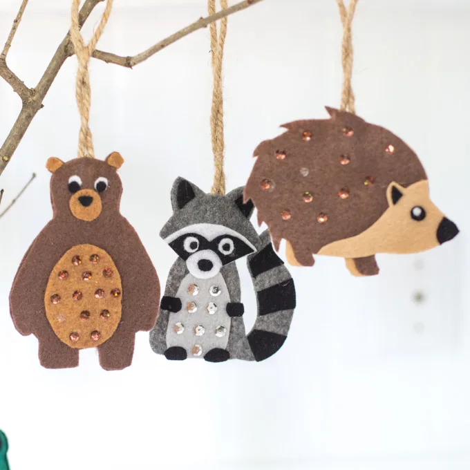Small felt ornaments hanging from a branch as woodland baby shower decorations including a bear, raccoon and hedgehog