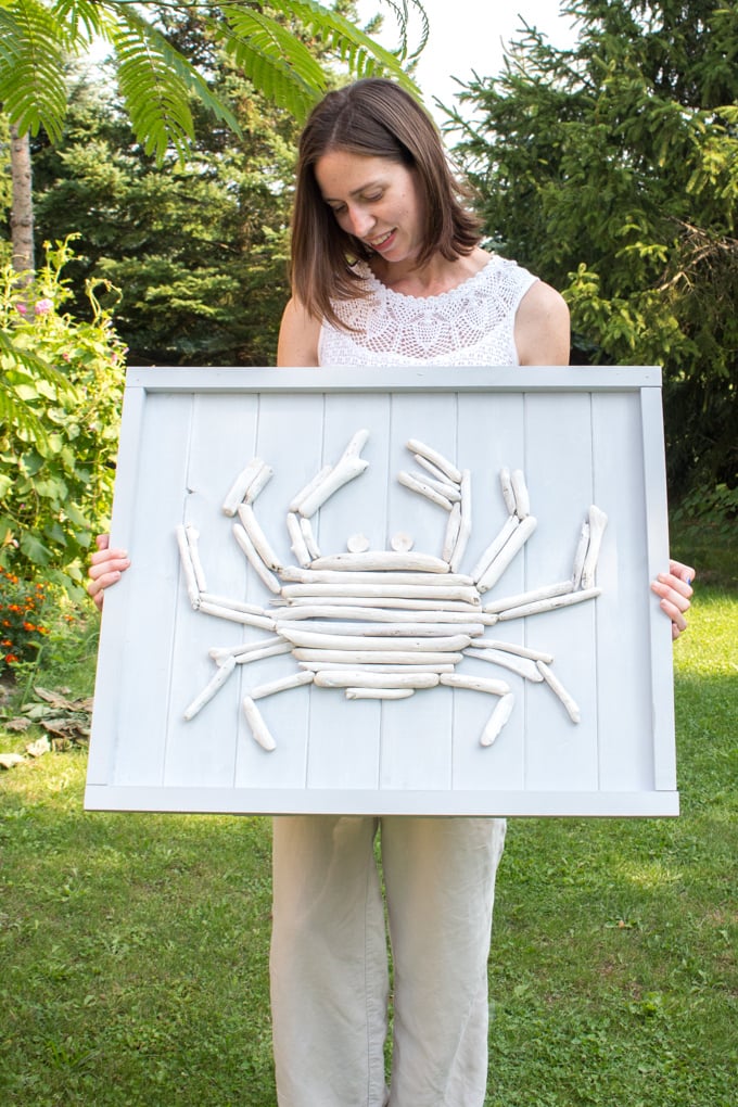 Woman standing outdoors holding a DIY driftwood crab wall art as an example of lake house decorating ideas