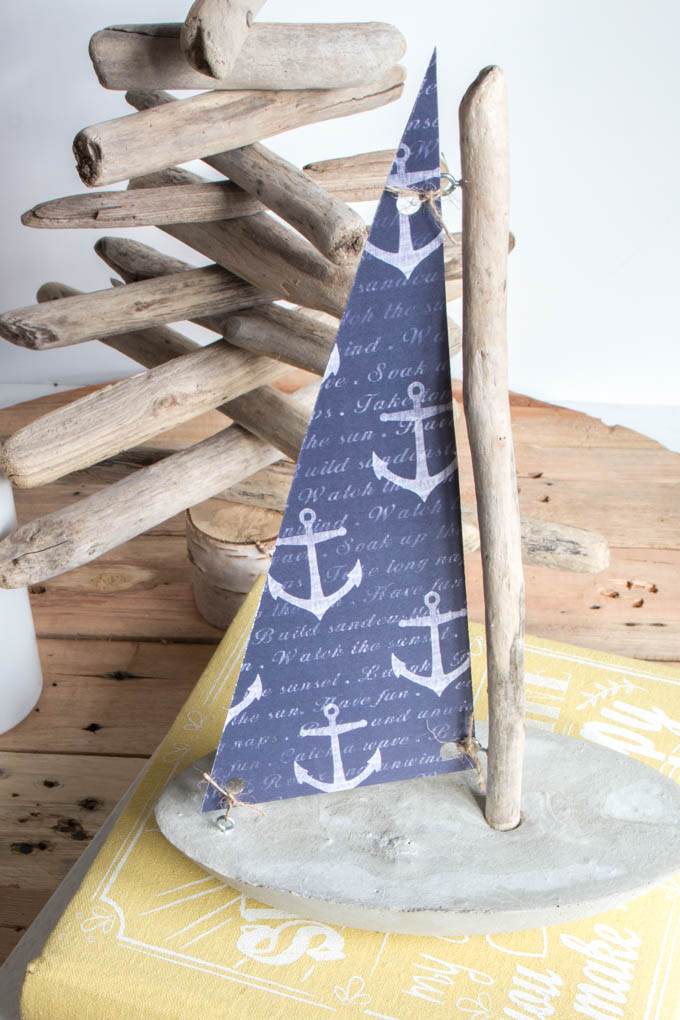 A decorative sailboat made with a concrete base, driftwood mast and nautical paper sail.