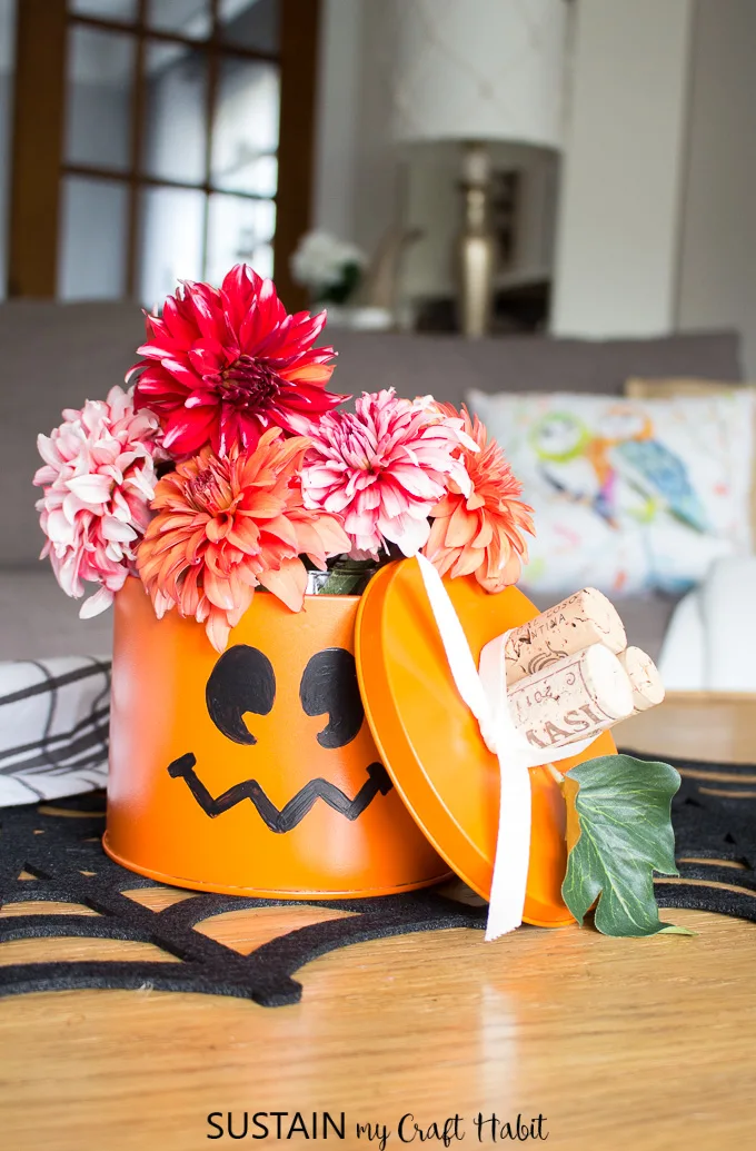 An old tin can, spray painted orange with a pumpkin face added on as an example of halloween decorating ideas