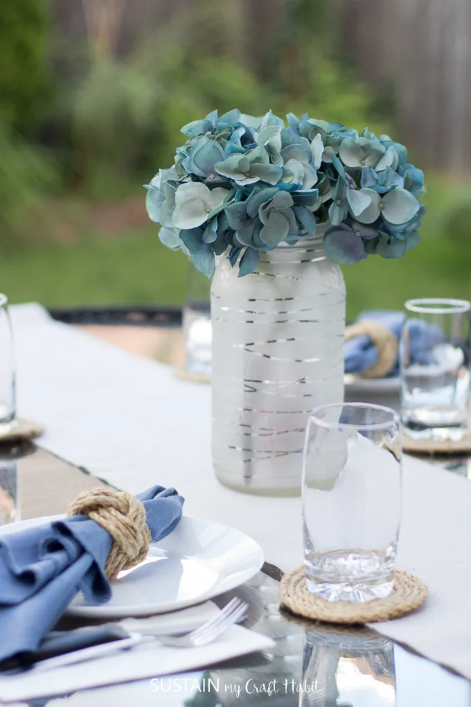 Frosted mason jar vase with blue silk hydrangeas on an outdoor patio table.