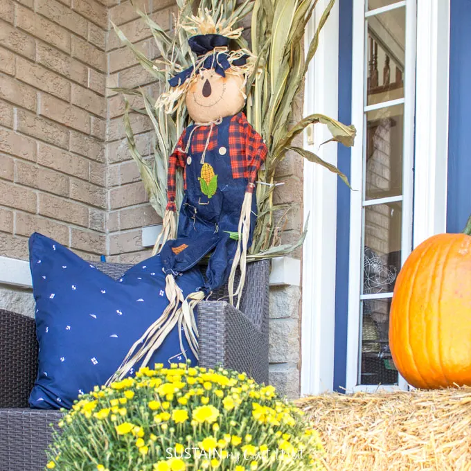 A scarecrow against cornstalks behind a chair on a fall front porch
