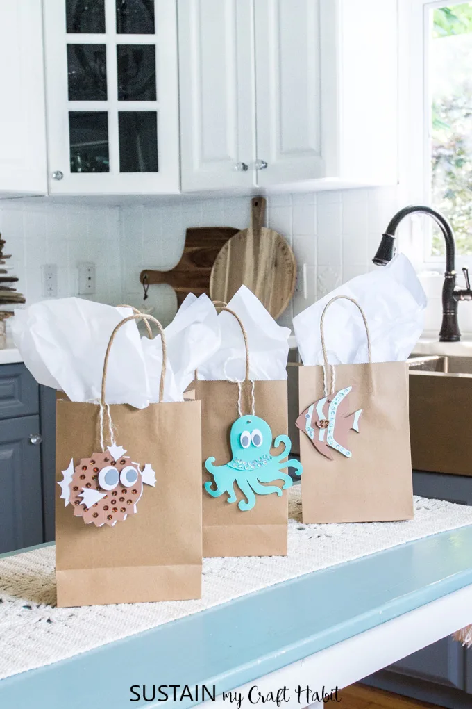 Set of three gift bags with white tissue paper and beachy printable gift tags including a puffer fish, octapus and clown fish