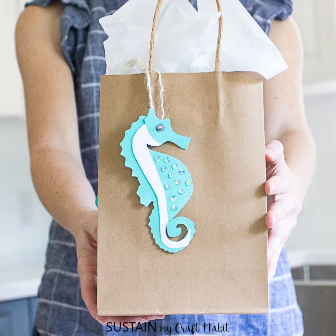 Woman holding gift bag with a beachy printable sea horse gift tag