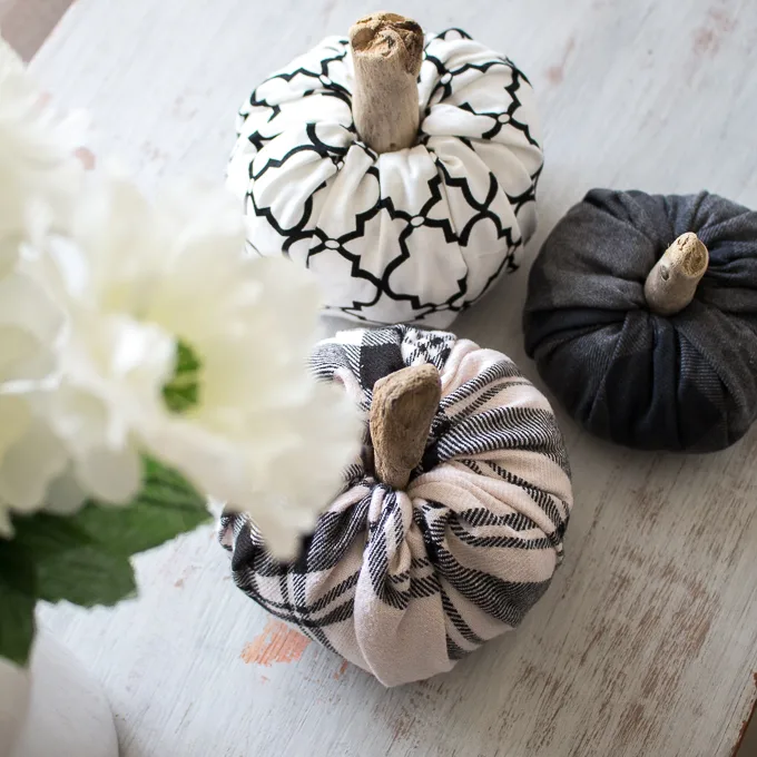 Overhead view of three fabric pumpkins of various sizes and patterns on a rustic wood surface.