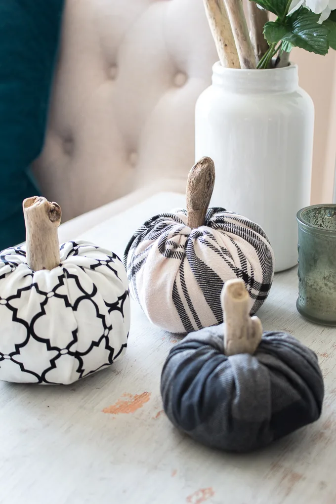 Three fabric pumpkins of different sizes make with scrap flannel and wood stems on a rustic wood surface. Neutral accessories surround the display.