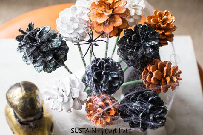 A view from above of black, gold and white painted pine cone flowers with faux spider webbing