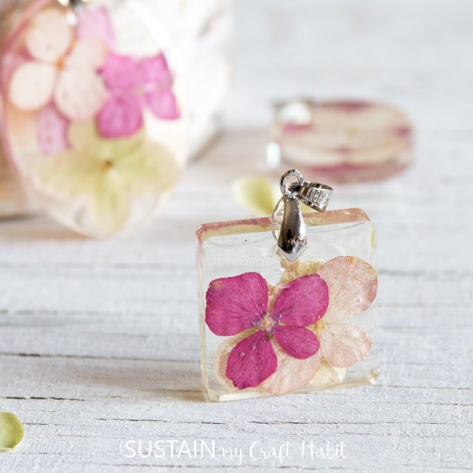 Close up image of a pressed pink hydrangea petals in a small square of clear resin. The pendant includes a silver bail for hanging onto a necklace.