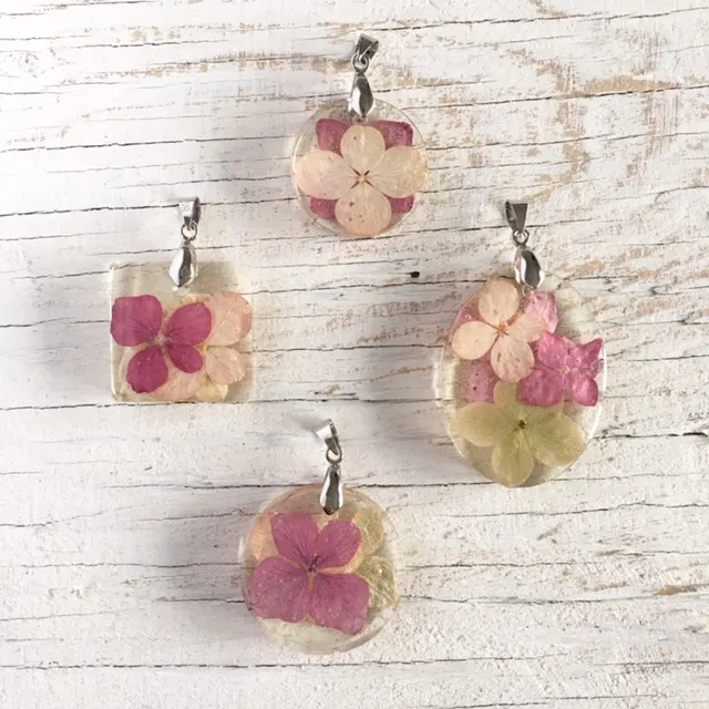 Overhead view of four completed resin pendants containing various colors and sizes of dried hydrangea flower petals. The pendants are arranged on a white wood surface.