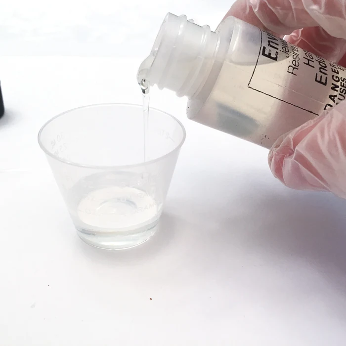 Pouring hardener from a small bottle into a small plastic measuring cup.