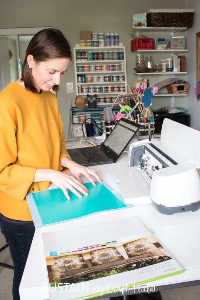 Sonya placing a sheet of turquoise vinyl onto a Cricut mat in preparation for feeding it into the Cricut Maker machine