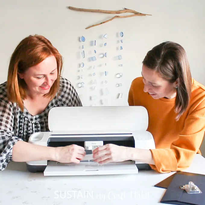 The post authors standing behind a Cricut Maker machine, looking at the mechanism inside.