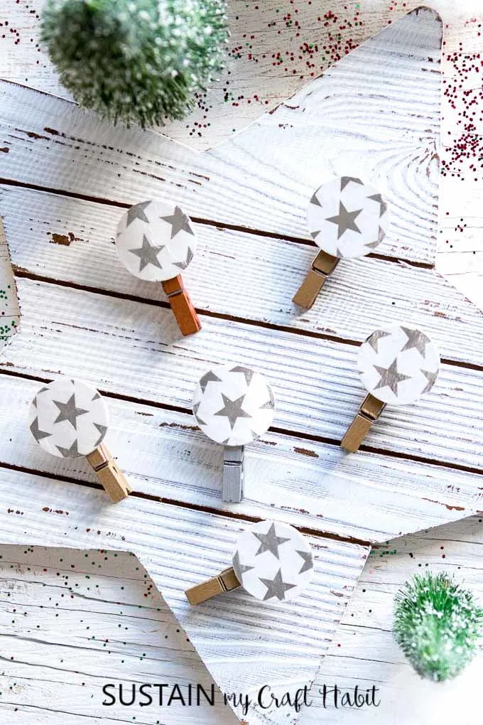 An arrangement of decorative clothespins, embellished with silver stars, laying on a rustic Christmas surface