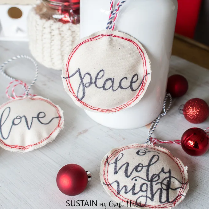 Three hand-lettered DIY Christmas ornaments on small canvases and gently stuffed