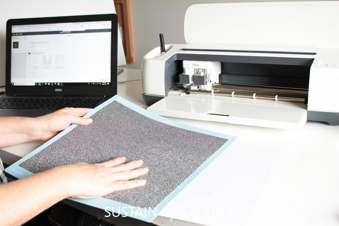 Placing black glitter vinyl into a light grip adhesive mat before placing it into a Cricut Maker machine