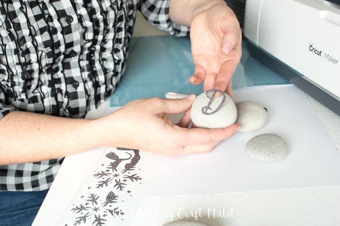 Woman placing the letter D, cut out from black glitter vinyl, onto a round beach stone.