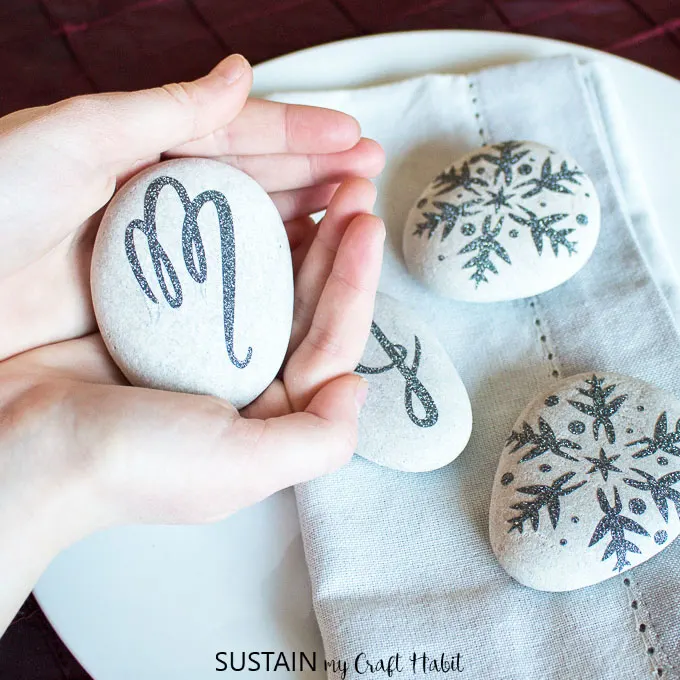 SO PRETTY! Create elegant monogrammed napkin weights with beach stones and some glitter vinyl. Perfect for a Christmas, New Year's Eve, wedding or bridal shower table setting. #cricutmaker #cricutcrafts #weddingtable #tablesetting #tablescape #newyearseveparty #rockcrafts #monogram #diy #napkinweights