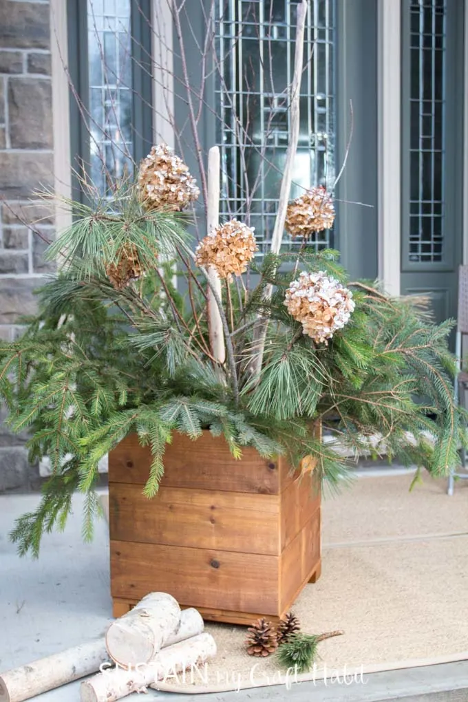 A cedar DIY planter box filled with pine greenery and branches on a front porch