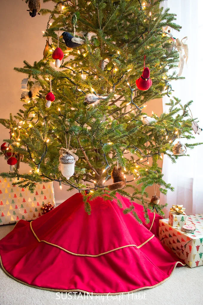 A red velour tree skirt with gold edging underneath a natural Christmas tree