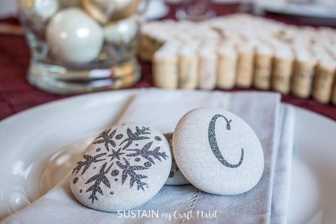 Beach stones embellished with delicate black glitter snowflakes and the letter C displayed on a napkin