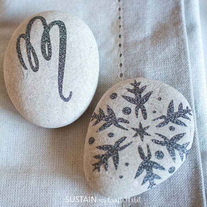 Close up image of two rocks embellished with a snowflake and monogram M using black adhesive glitter vinyl from Cricut