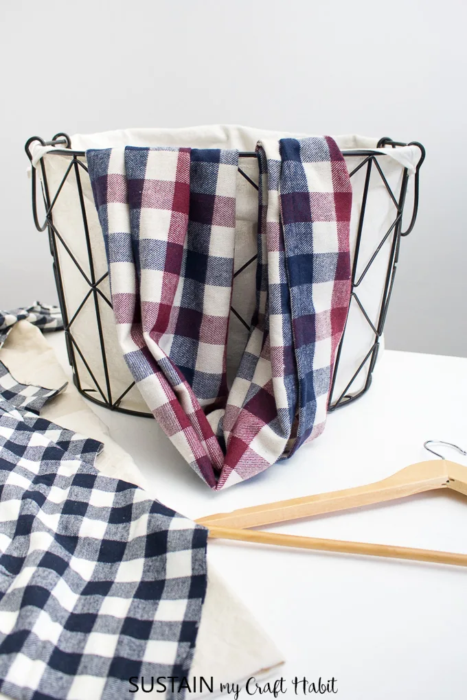 Beautiful handmade burgundy and blue plaid infinity scarf draped over a farmhouse style basket as an example for this how to sew an infinity scarf tutorial