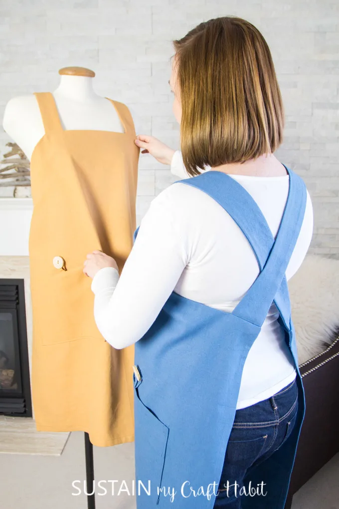Woman wearing a blue cotton utility apron hanging a mustard colored one made from a DIY apron pattern