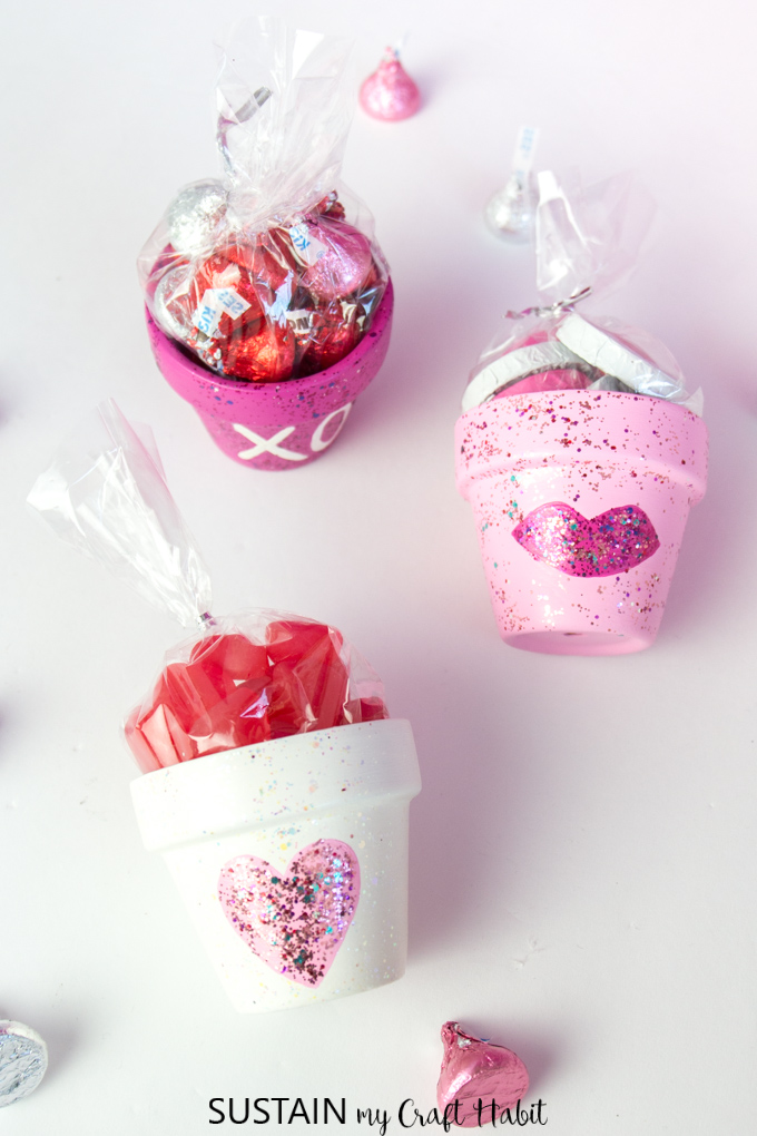 Three small clay pots, painted in pinks and white then filled with sweet treats, displayed on a white surface