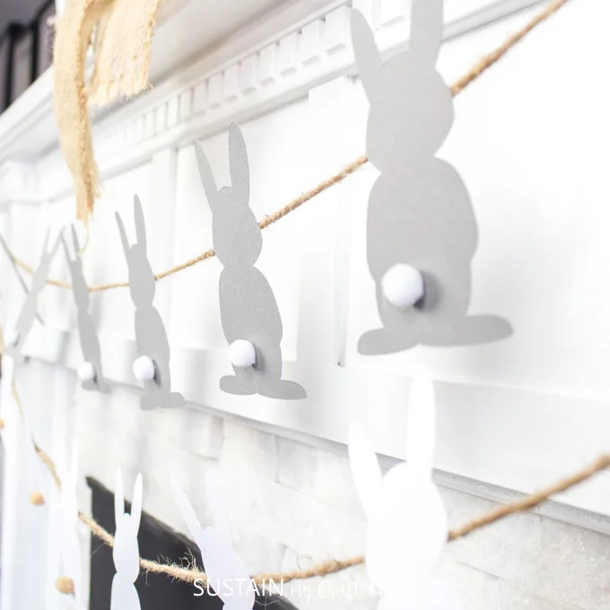 Close up image of the the gray bunnies with white pom pom tails strung along twine to make the Easter garland.