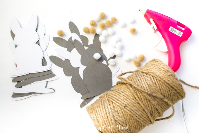Supplies needed to make the DIY Easter garland including twine, hot glue gun, pom poms and bunny cut-outs.