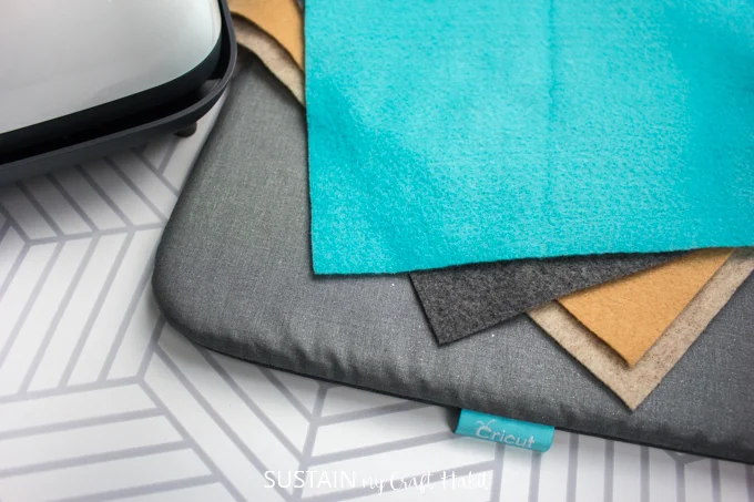 Teal, gray and mustard colored felt fabric on top of a Cricut heat press mat.