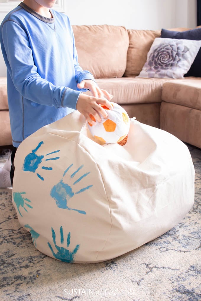 Boy placing a plush ball inside a storage ottoman sewed with canvas fabric