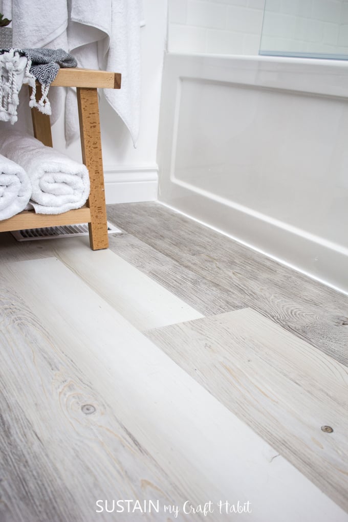 A close up image of the frosted gray multi-width Lifeproof vinyl plank flooring, installed in a bathroom with wooden accessories in the background.