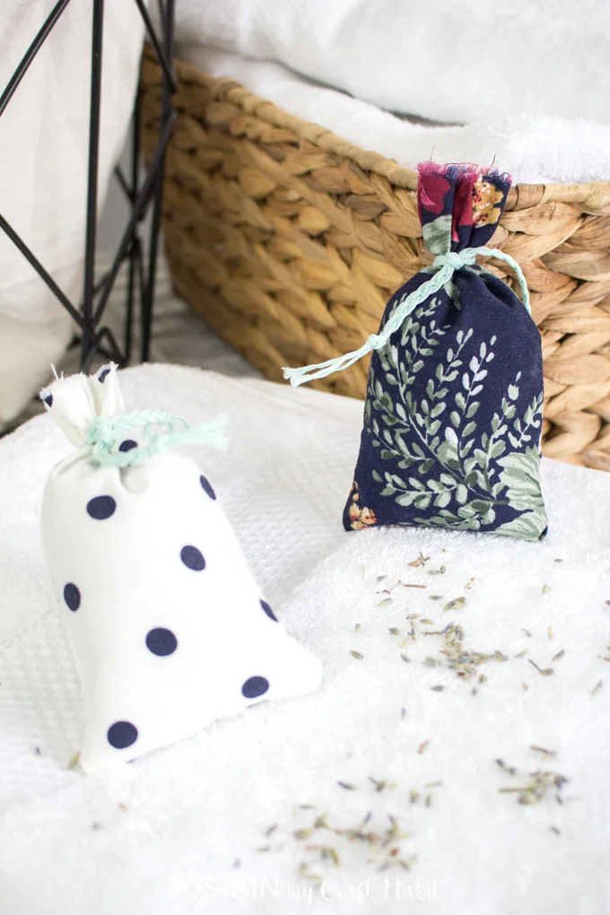 Two finished lavender sachets on a white cloth surface with a rustic basket in the background.