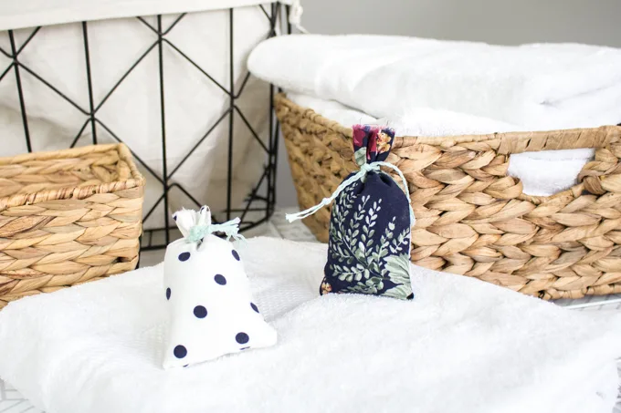 Two finished scented sachets with farmhouse style decorative elements in the background including baskets and linens.