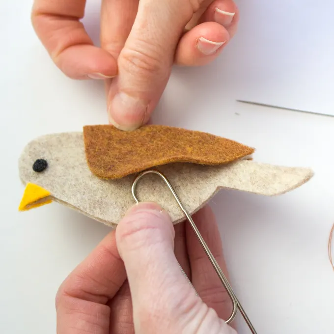 Positioning the large paper clip under the felt bird's wing prior to sewing it in place.