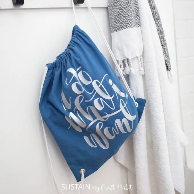 A DIY drawstring bag, with vinyl lettering, hanging from a hook against a white wall.