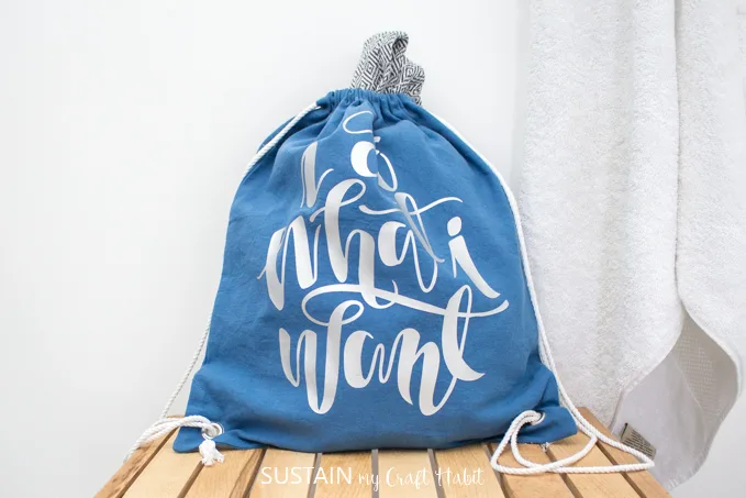 A drawstring cinch bag, made from blue canvas fabric and white drawstring cord with the phrase "I do what I want" pressed onto it with silver vinyl.