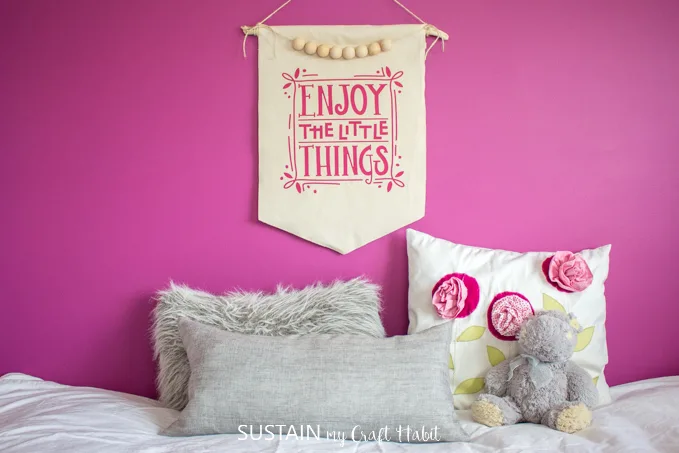 A DIY canvas wall hanging from canvas fabric and driftwood on a magenta pink wall