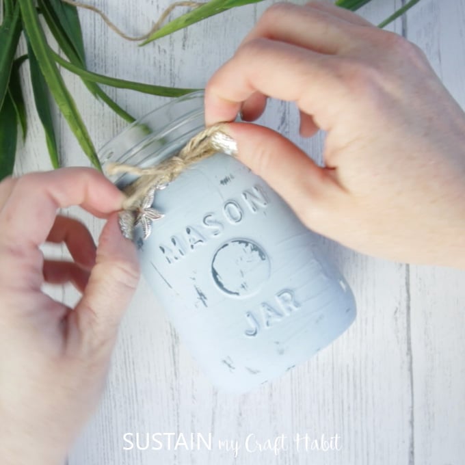 Tying the twine around the neck of the painted mason jar.
