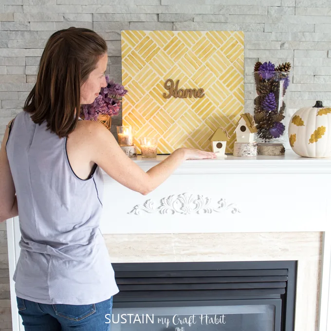 Woman placing autumn decorating elements onto a fireplace mantle.