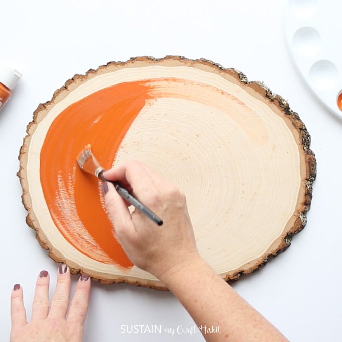 Woman starting to paint one surface of the wood slice with orange chalky paint.