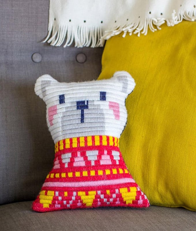 A pillow in the shape of a white bear wearing a red sweater.