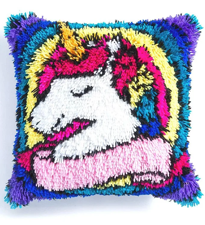 A square pillow made with yarn and with a unicorn image on the front.