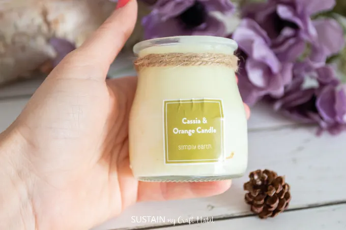 Hand holding a finished DIY fall candle in the jar with a green label reading Cassia and Orange Candle.