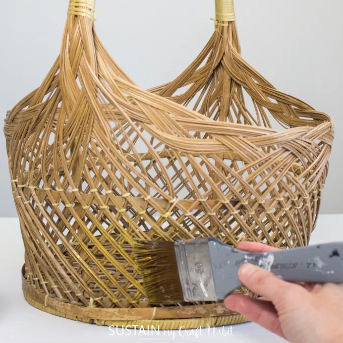A hand painting the bottom of wicker basket with gold paint.
