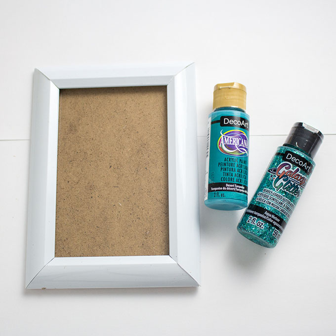 While photo frame beside bottle of turquoise craft paint.