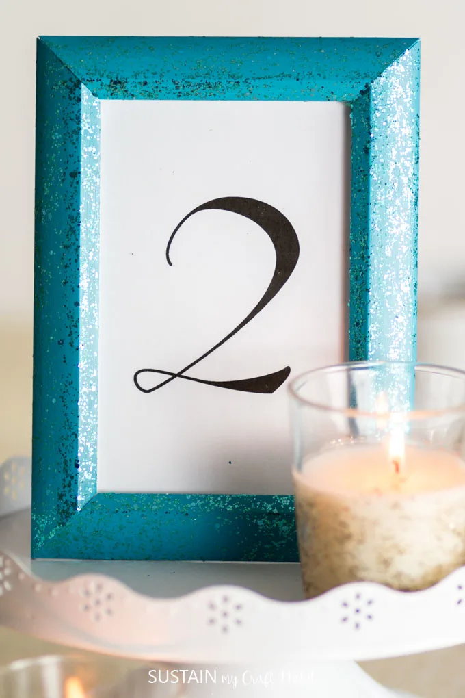 Close up view of the completed elegant  wedding table decorations including a turquoise frame with the number 2, and a small candle.